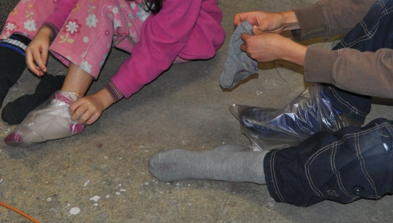 Über die Socken ziehen die Kinder Plastiksäcke an und darüber "alte" Socken. So können sie in Farbe treten.
